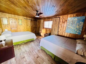 A room with two beds, a wooden ceiling, a ceiling fan, a window with curtains, and a wall-mounted painting. - Newly Renovated Cottage Stoney Lake (Douro-Dummer)