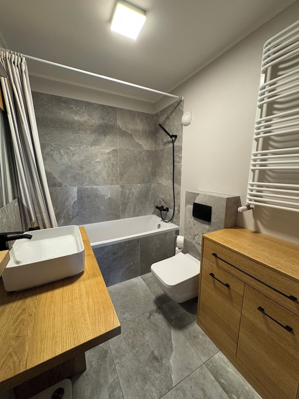 Ein modernes Badezimmer mit einer Badewanne, einem Holzwaschtisch und einer Toilette.