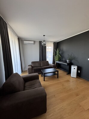 Ein modernes Wohnzimmer mit einer Couch, einem Couchtisch, einem Klavier und einer Topfpflanze.