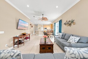 Ein Wohnzimmer mit einer Couch, einem Couchtisch und einem Fernseher. Im Hintergrund ist eine Küche zu sehen.