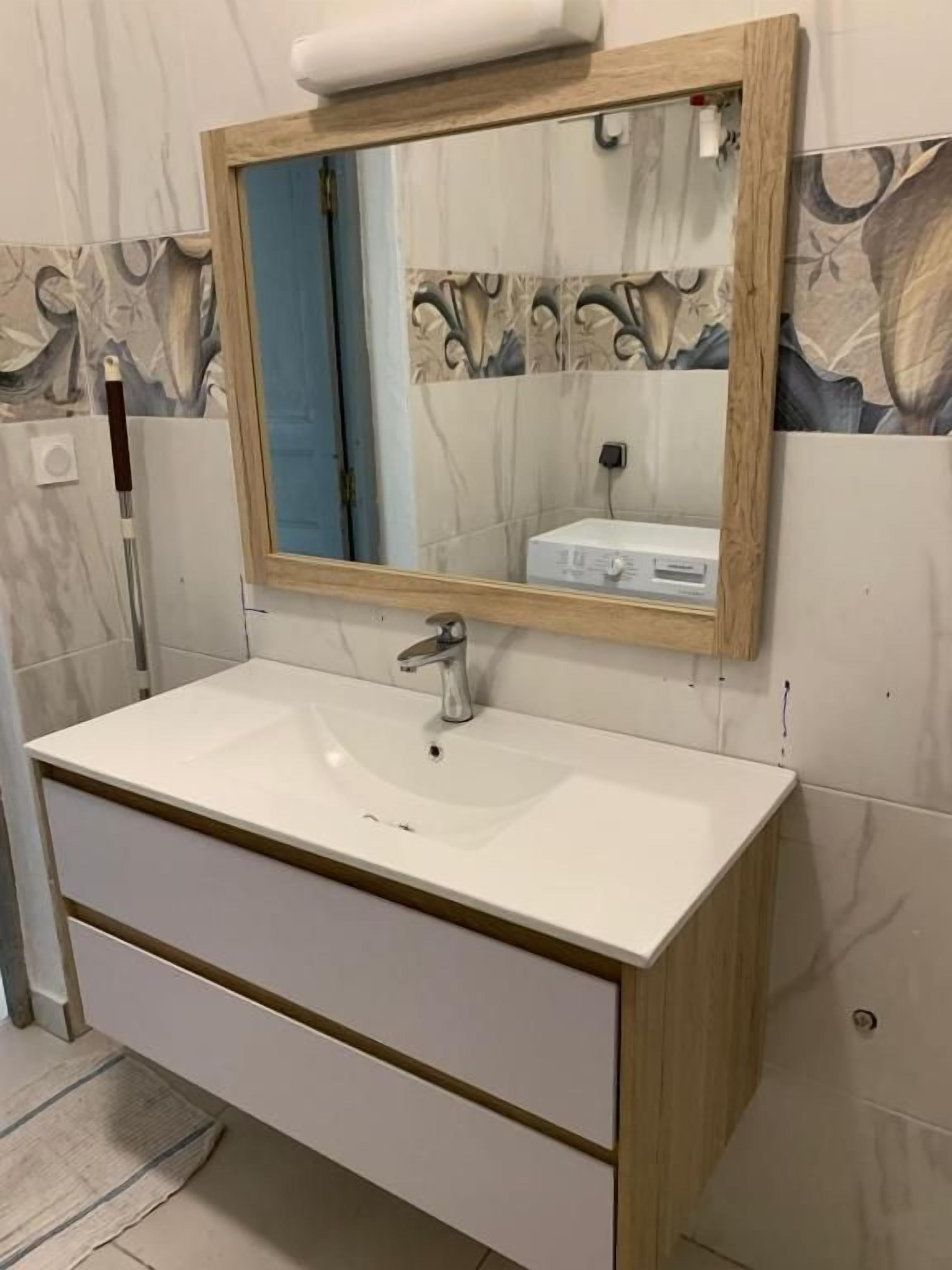 A bathroom with a white sink, a wooden-framed mirror, and a patterned wall.