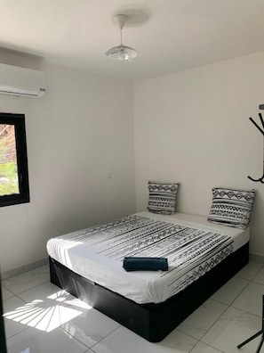 Una habitación con cama, ventana y ventilador de techo.