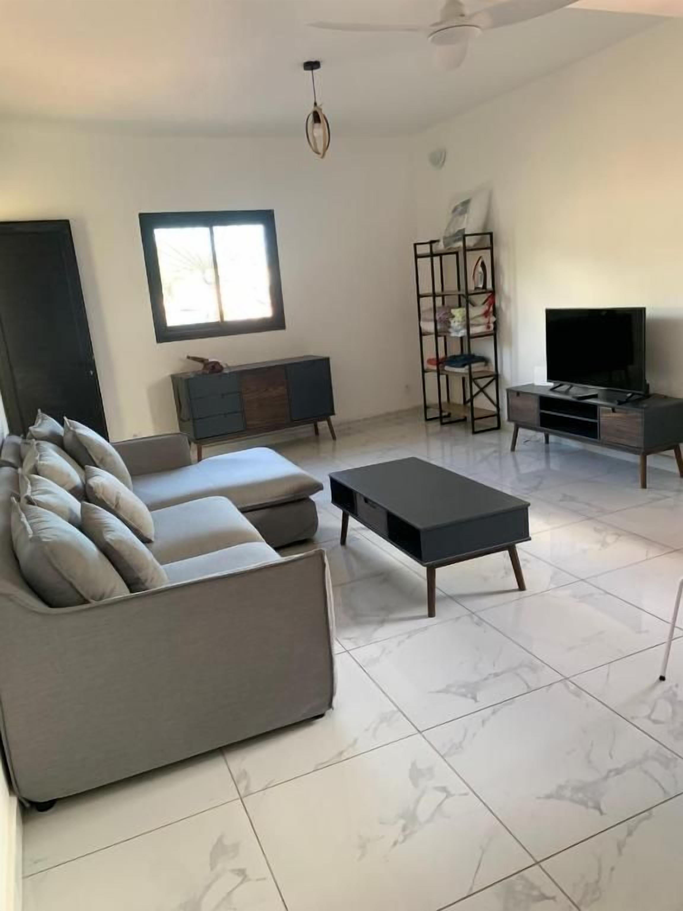 A modern living room with a grey sofa, a black coffee table, a TV stand, and a bookshelf.