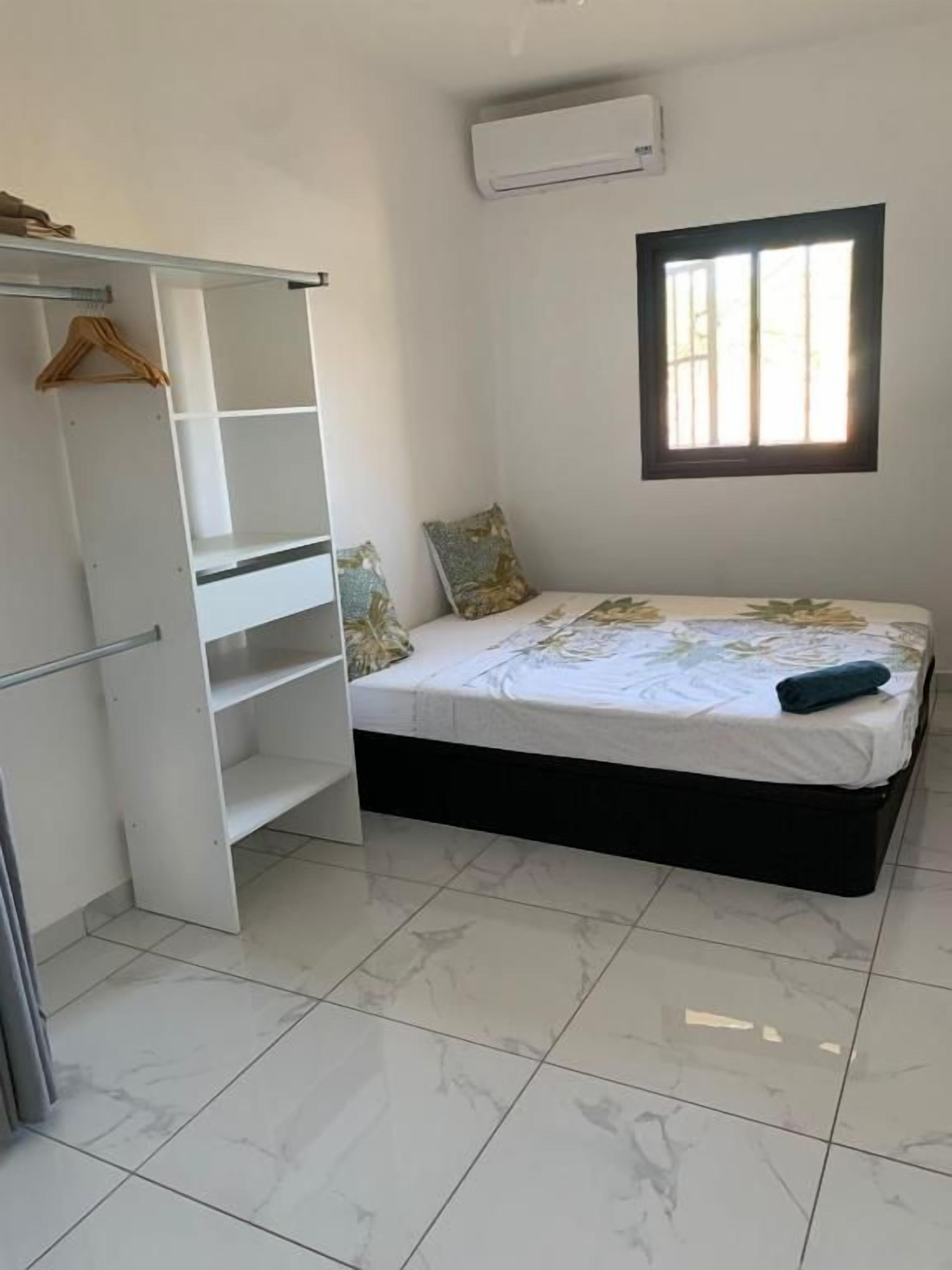 A bedroom with a bed, a wardrobe, a window, and an air conditioning unit.