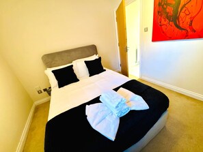 A neatly made bed with white and black bedding, a gray headboard, and a folded towel on the bed. - Modern Finnieston 2 Bed Apt, near SEC & OVO, Free Parking (Glasgow)