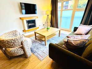 A living room with a sofa, armchair, coffee table, fireplace, TV, and a view of the outdoors. - Modern Finnieston 2 Bed Apt, near SEC & OVO, Free Parking (Glasgow)