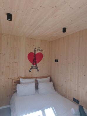A wooden-paneled room with a bed, a wall-mounted light fixture, and a Paris-themed design including the Eiffel Tower and a heart.