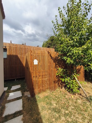A wooden fence with a mailbox, a paved path, and a tree with green leaves.