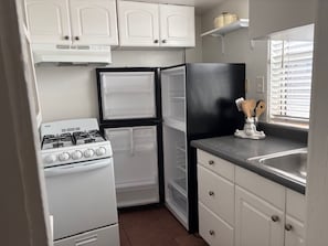 A compact kitchen with white cabinets, a black refrigerator, a gas stove, and a window with blinds.