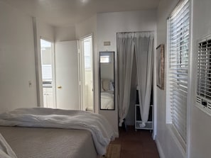 Une chambre à coucher avec un lit, un miroir, une porte et une fenêtre avec des stores.