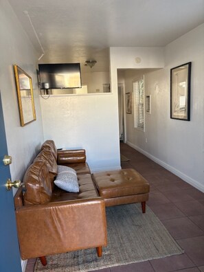 A living room with a brown leather sectional sofa, a flat-screen TV mounted on the wall, and a hallway leading to other rooms. - Cozy, comfy w/ private court yard in the heart of Chula Vista (Chula Vista)