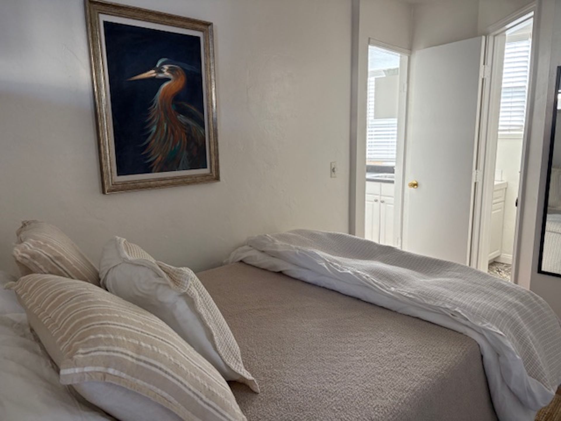 A bedroom with a bed, pillows, a painting, and a door leading to a balcony.