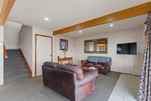 A living room with a sofa, a coffee table, a TV, and a staircase. - Fern View - Pukawa Bay Holiday Home (Turangi)