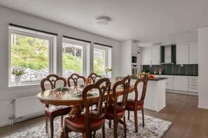 Une cuisine moderne avec des meubles blancs, un coin repas avec des chaises en bois et une vue sur la verdure à l’extérieur.