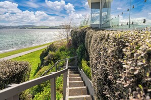A staircase leading down to a waterfront area with a clear view of the sea and a distant cityscape. - Hampton Cottage by the Lake - Taupo Holiday Home (Taupo)