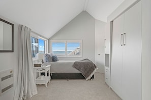 A bedroom with a bed, a desk, a chair, a window with a view of the sea, and a wardrobe. - Hampton Cottage by the Lake - Taupo Holiday Home (Taupo)