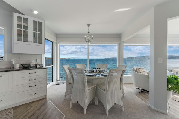 A modern kitchen with white cabinetry and a dining area with wicker chairs and a view of the sea. - Hampton Cottage by the Lake - Taupo Holiday Home (Taupo)