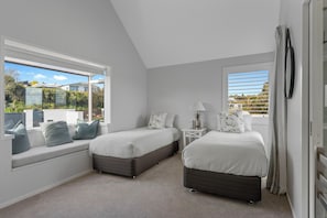 A bedroom with two beds, a window seat, and a view of the outside. - Hampton Cottage by the Lake - Taupo Holiday Home (Taupo)