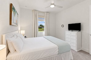 Ein Hotelzimmer mit einem Bett, einem Fernseher auf einer Kommode, einem Deckenventilator und einem Fenster mit Vorhängen.