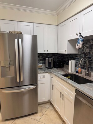 A kitchen with white cabinets, a stainless steel refrigerator, a coffee maker, and a sink with a marble countertop. - Waterfront Condo in Indian Shores- Beach - Pool - Boat Slips (Indian Shores)