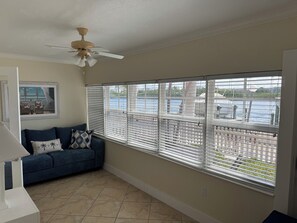 A room with a blue sofa, a ceiling fan, a window with blinds, and a view of a body of water. - Waterfront Condo in Indian Shores- Beach - Pool - Boat Slips (Indian Shores)