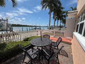 Eine Terrasse mit rundem Tisch und Stühlen, ein weißer Zierzaun und Blick auf das Wasser und Boote.