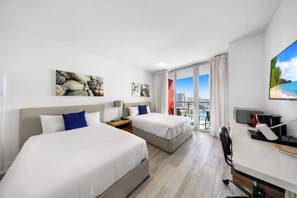A hotel room with two beds, a desk, a TV, and a balcony with a city view. - Beachwalk Resort 2 BDR Family-Friendly (Hallandale Beach)