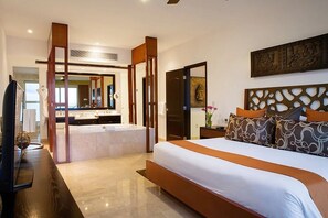 A modern hotel room with a large bed, a bathroom with a bathtub, and a television on a wooden table. - Two-Story Penthouse Loft, 3-bdrm Beachfront at Villa del Palmar Luxury Resort (Cancun)