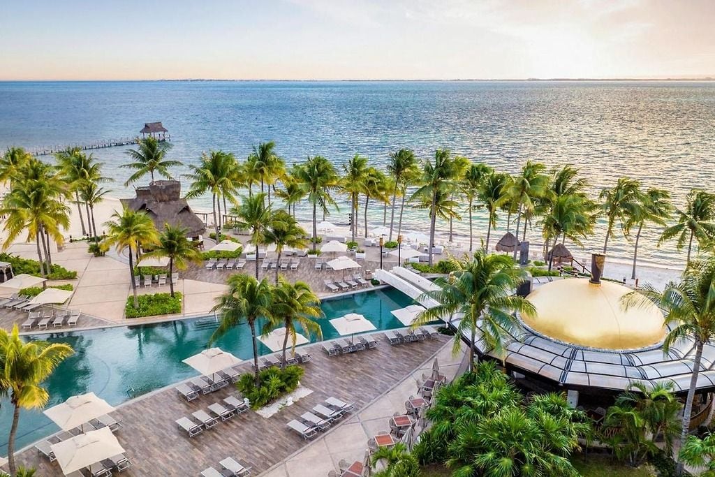 Un resort con piscina, palme e vista sull'oceano.