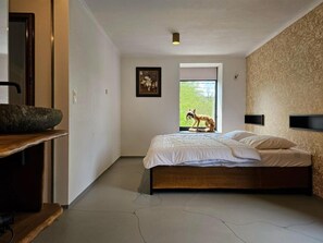 Ein Schlafzimmer mit einem Bett, einem Steinkonstruktion-Becken, einem gerahmten Bild, einem Fenster und einer Wandleuchte.
