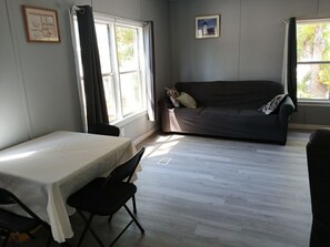 A room with a bed, a table, and a couch. There are windows with curtains, a picture on the wall, and a door. - Beautiful 3-bedroom mobile home with AC in Port Orange (Port Orange)