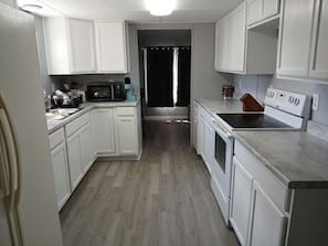 A kitchen with white cabinets, a microwave, a stove, and a sink. - Beautiful 3-bedroom mobile home with AC in Port Orange (Port Orange)