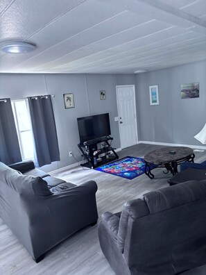 A living room with a flat-screen TV, two sofas, a coffee table, and a patterned rug. - Beautiful 3-bedroom mobile home with AC in Port Orange (Port Orange)