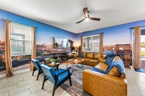 A living room with a cityscape mural, a ceiling fan, a sofa, a coffee table, and a TV. - Sleeps 24 - Pool-Game Room-Disney-Cinema Room (Davenport)