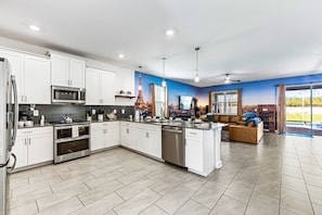 A modern kitchen with white cabinetry, a central island, and a dining area with a sofa and TV. - Sleeps 24 - Pool-Game Room-Disney-Cinema Room (Davenport)
