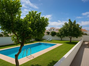Ein rechteckiger Swimmingpool mit Leiter, umgeben von einem gepflegten Rasen und Bäumen.