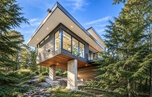 A modern house with a wooden deck, large windows, and a stone foundation. - Sleek 5 bed 4 bath Modern cottage on Lake Muskoka (Gravenhurst)