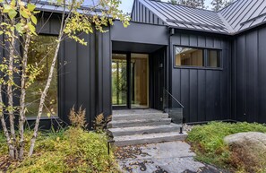 Een modern gebouw met een donkere gevel, een glazen deuropening en een stenen trap naar de ingang.