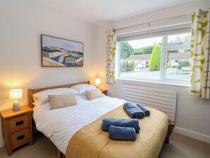 A bedroom with a bed, two bedside lamps, a window with curtains, a radiator, and a painting on the wall. - Hillset View (Bakewell)