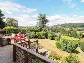 Une terrasse en bois offrant une vue sur un jardin aménagé et sur des collines lointaines.