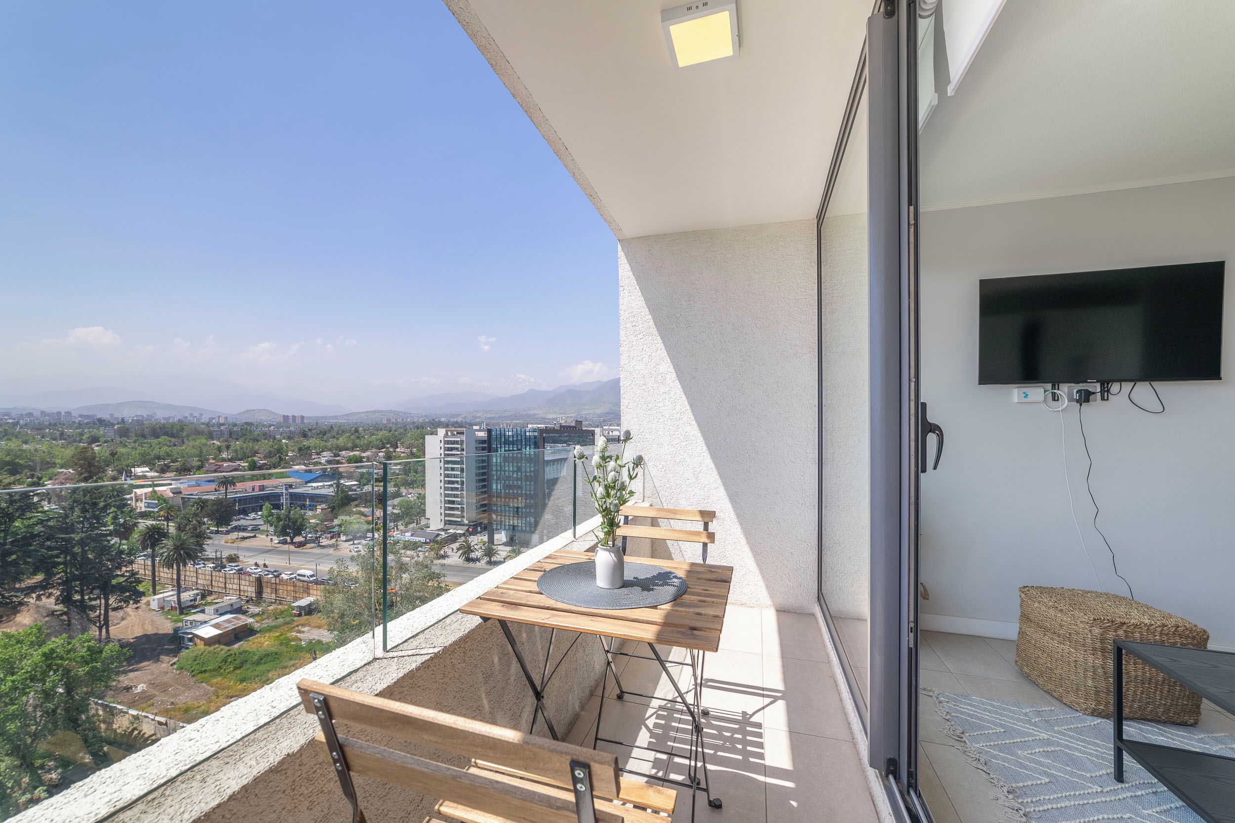 A balcony with a wooden table, a potted plant, and a TV mounted on the wall.