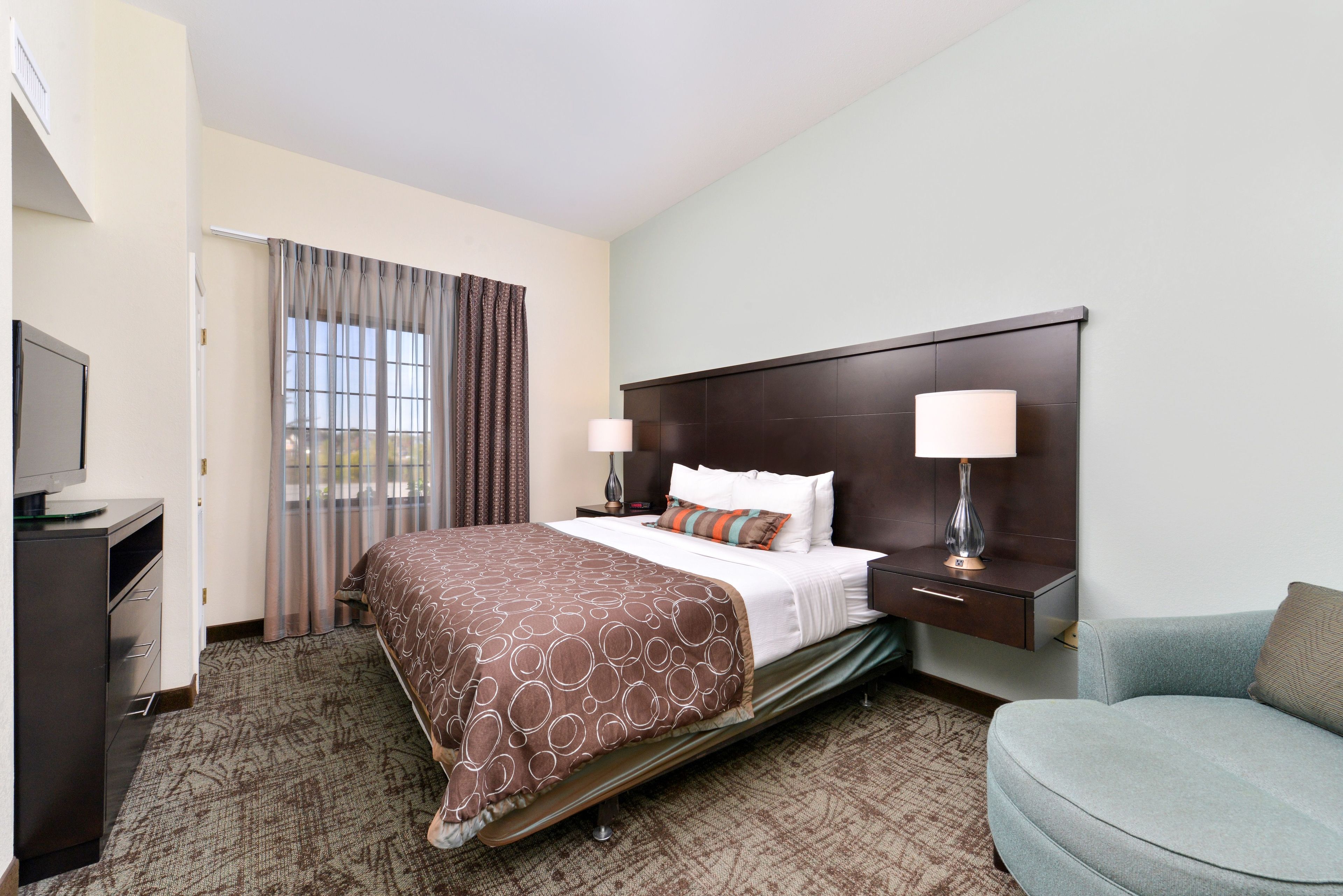 A hotel room with a bed, bedside tables, a TV, a desk, and a chair.