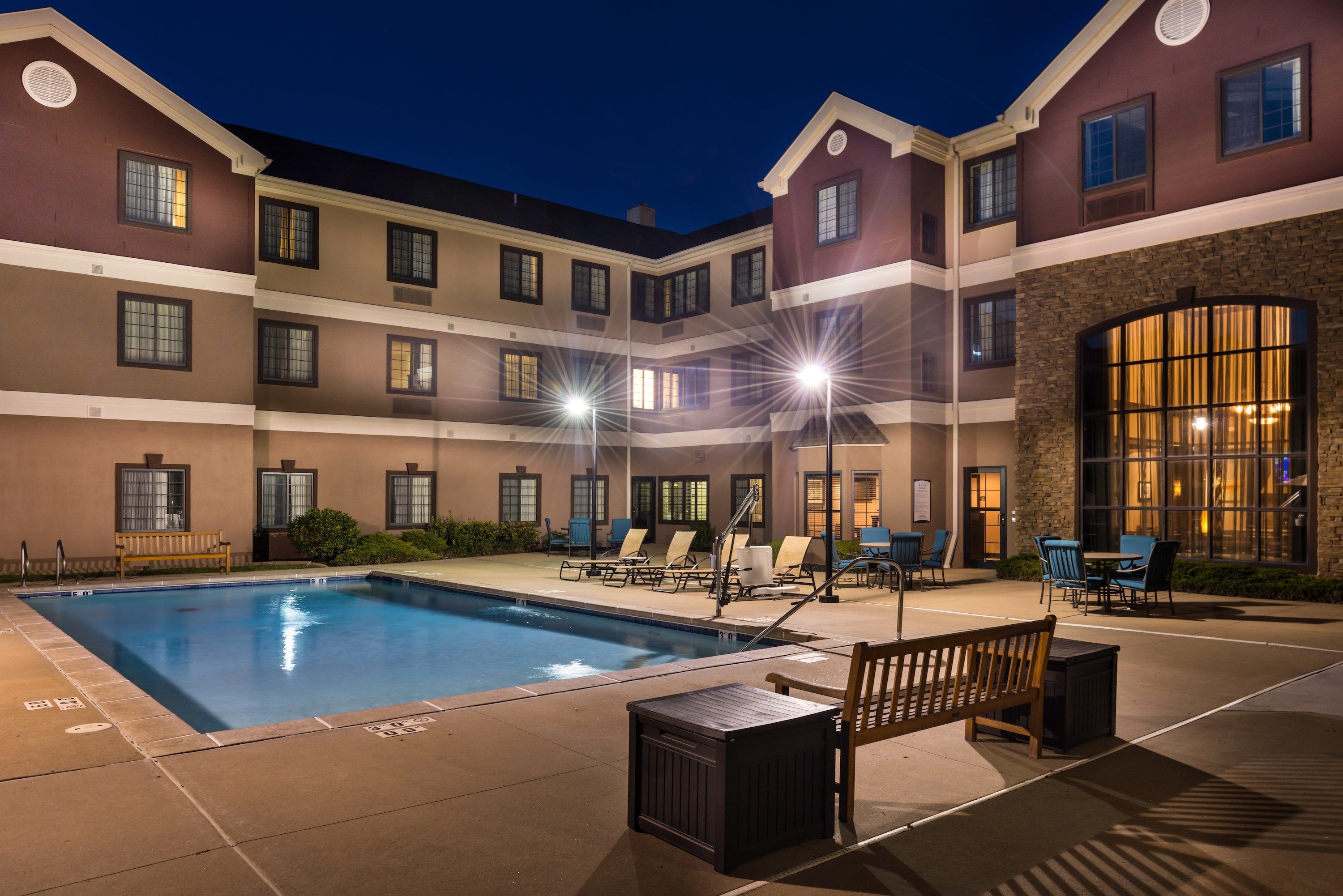 A hotel pool area with a rectangular pool, lounge chairs, and a wooden bench.