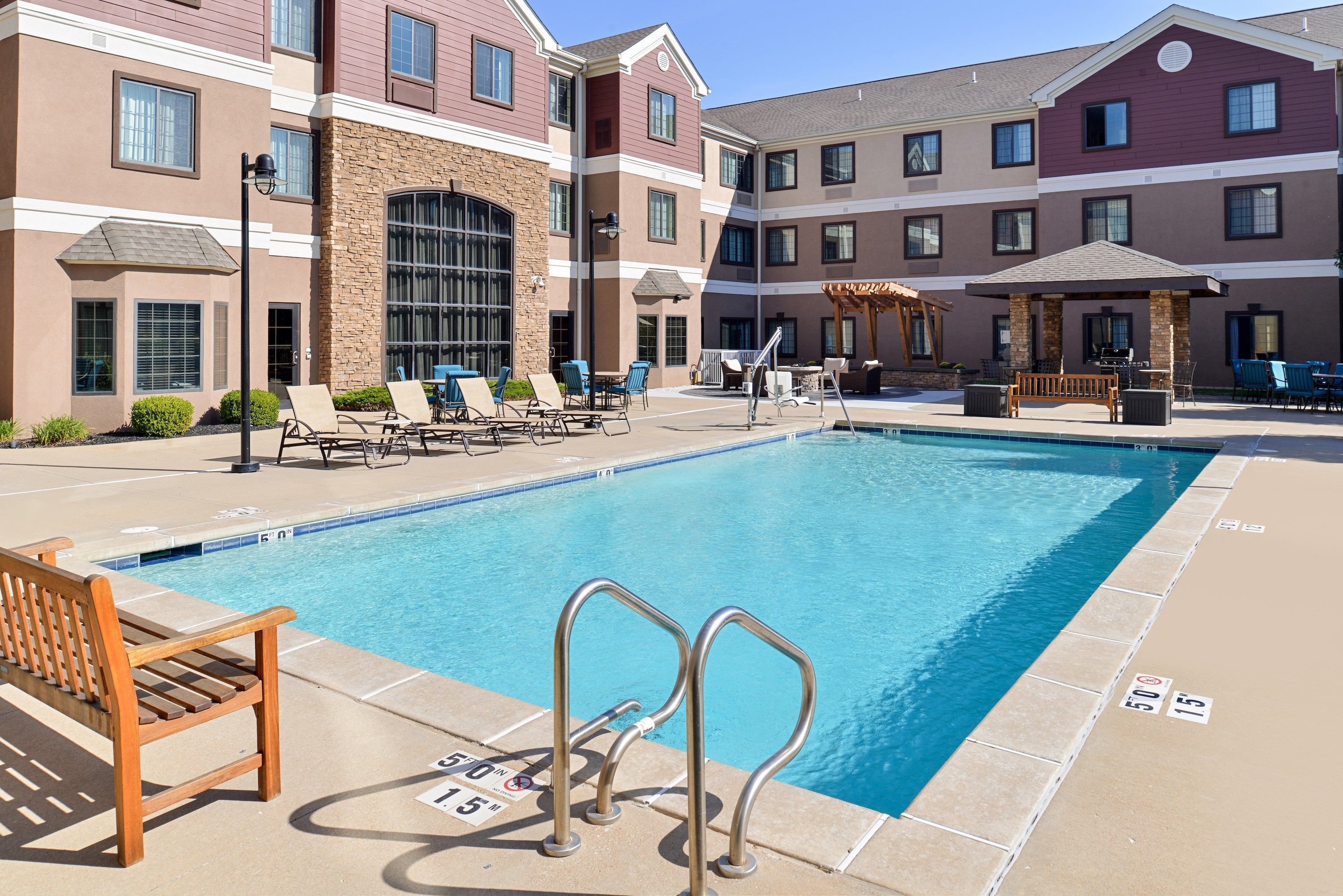 A pool area with lounge chairs, a wooden bench, and a covered seating area.