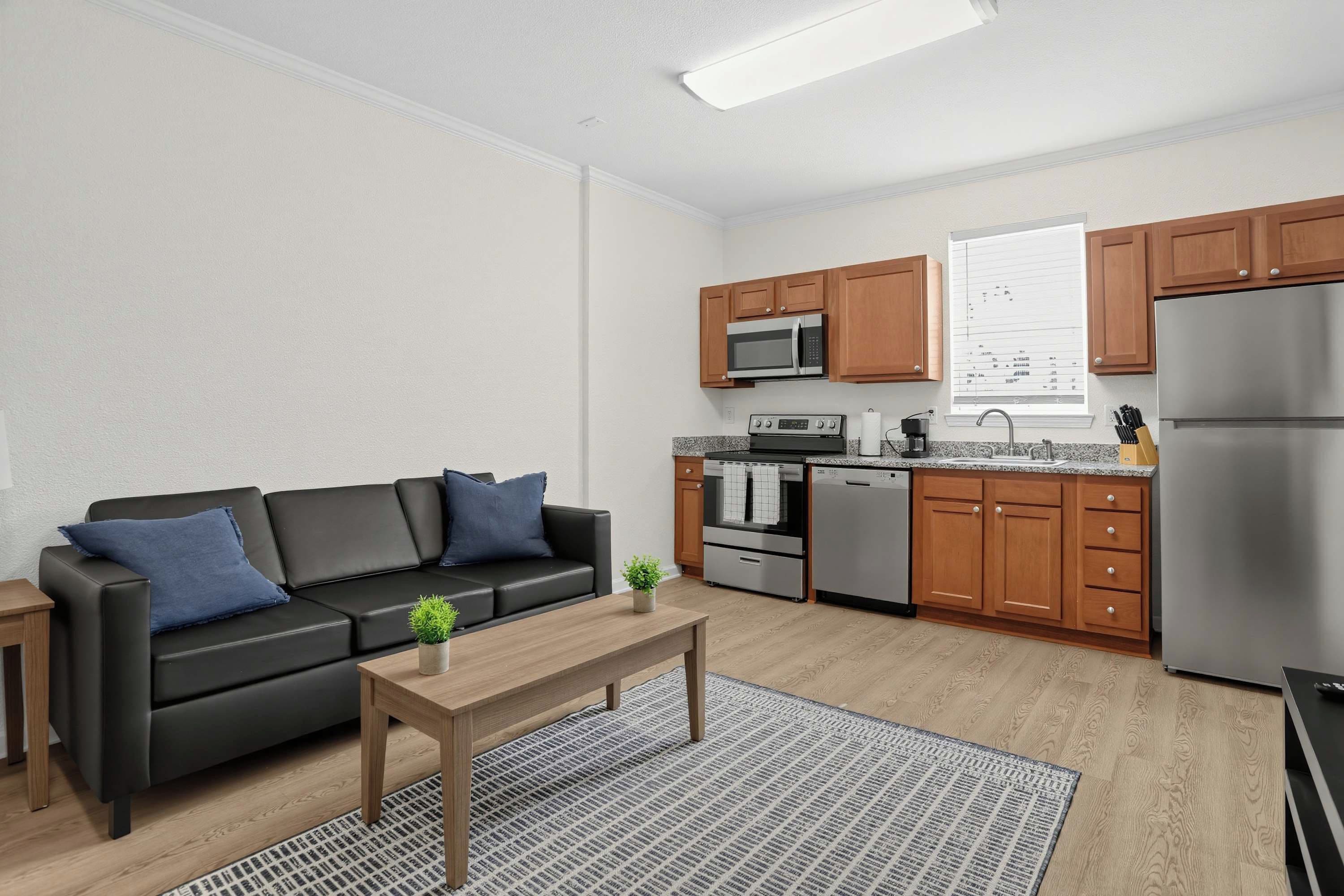 Une cuisine moderne dotée d’appareils électroménagers en acier inoxydable, de meubles en bois et d’un canapé en cuir noir agrémenté de coussins bleus.