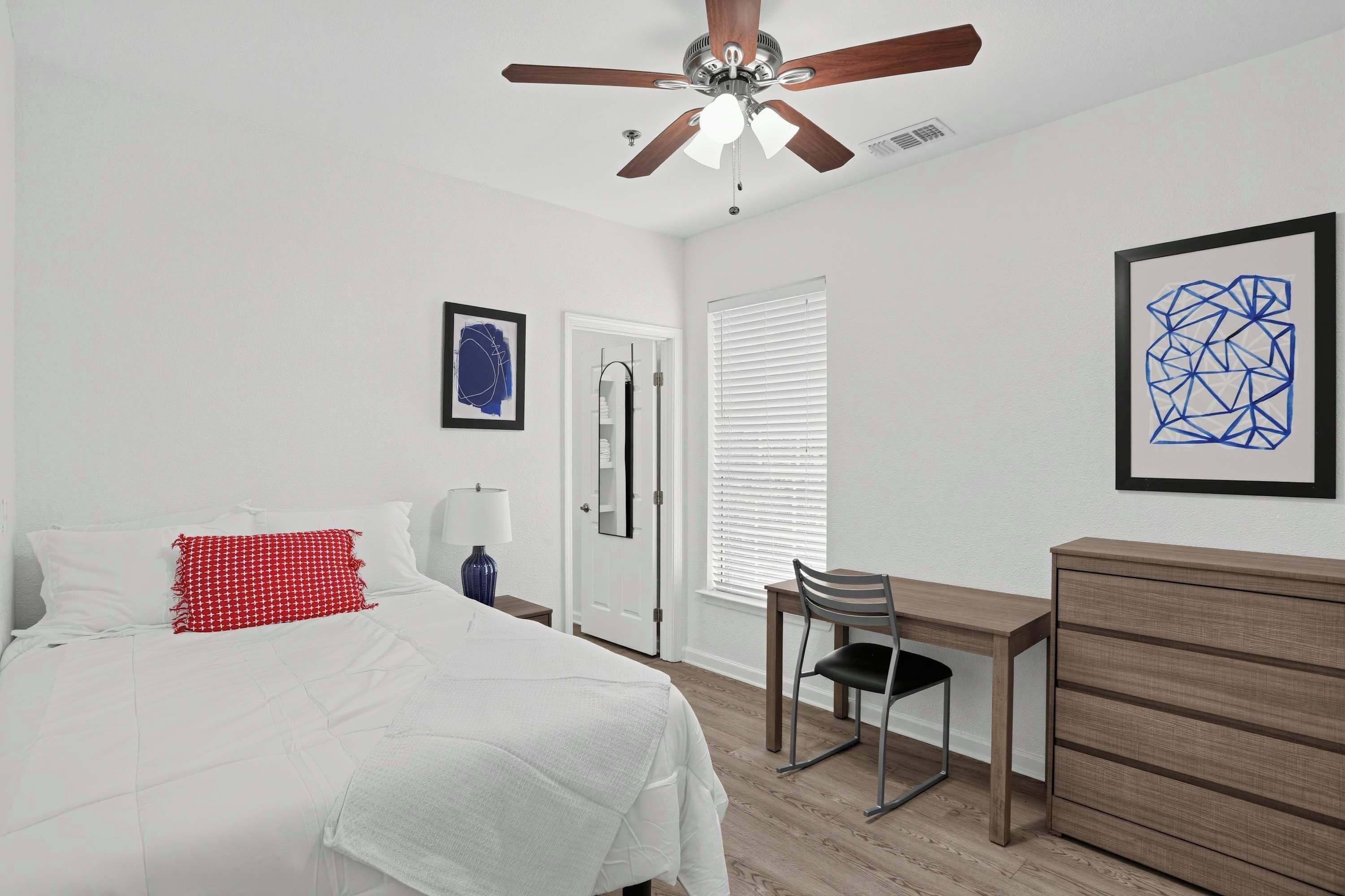 Ein Schlafzimmer mit Bett, Schreibtisch, Stuhl, Kommode und Deckenventilator.