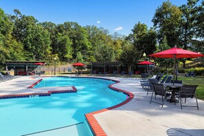 A swimming pool with a red border, surrounded by lounge chairs and umbrellas, set against a backdrop of trees.