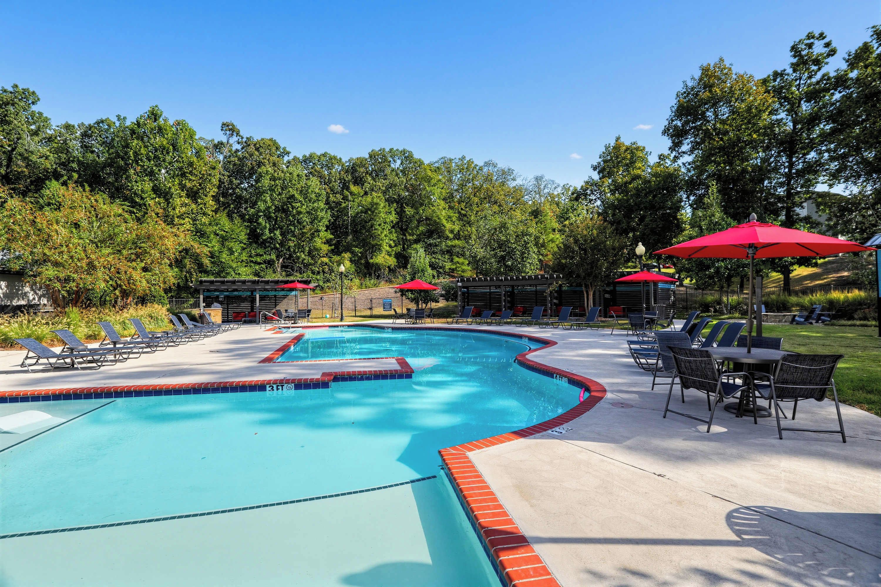 A swimming pool with a 3ft depth marker, surrounded by lounge chairs and umbrellas, with a forested background.