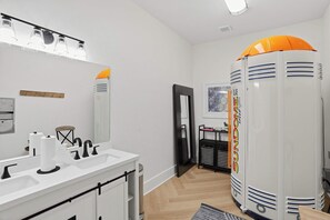 Un baño moderno con un lavamanos blanco, grifos negros y un espejo. Hay un toallero sobre el lavamanos y un inodoro con marco negro.