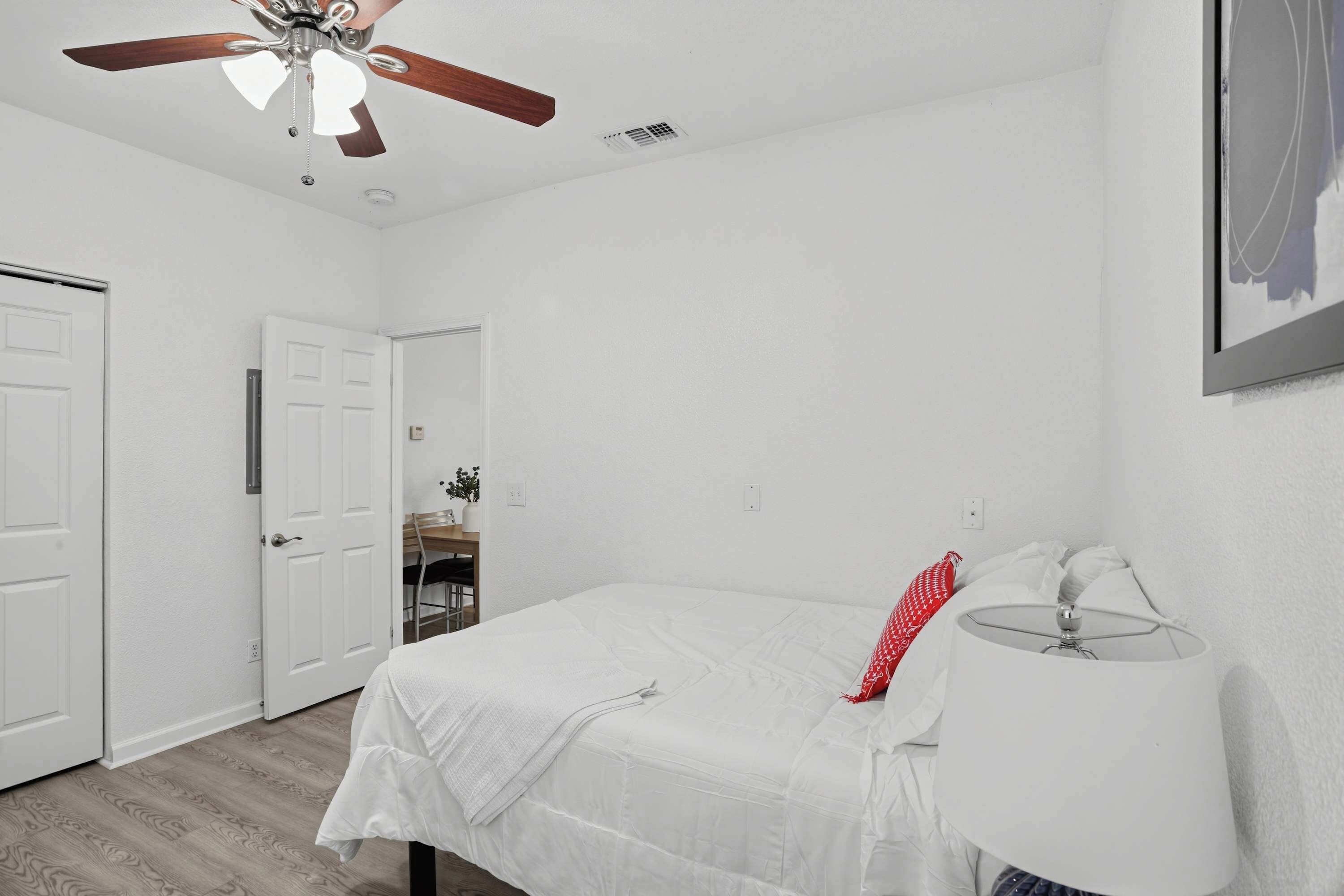 Quarto com cama, abajur, ventilador de teto e porta para outro cômodo.